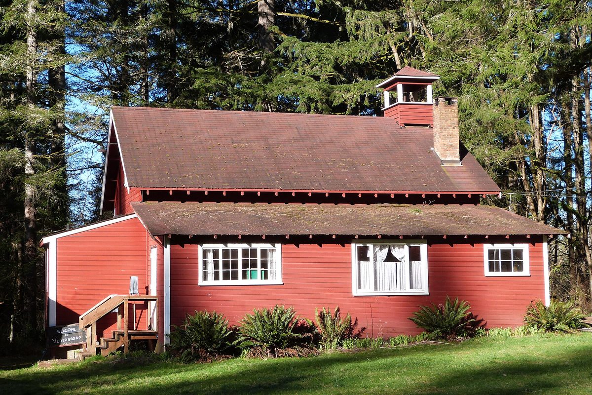 The red wooden Venersborg School, built in 1912, with a small bell tower, standing among tall evergreens near Battle Ground