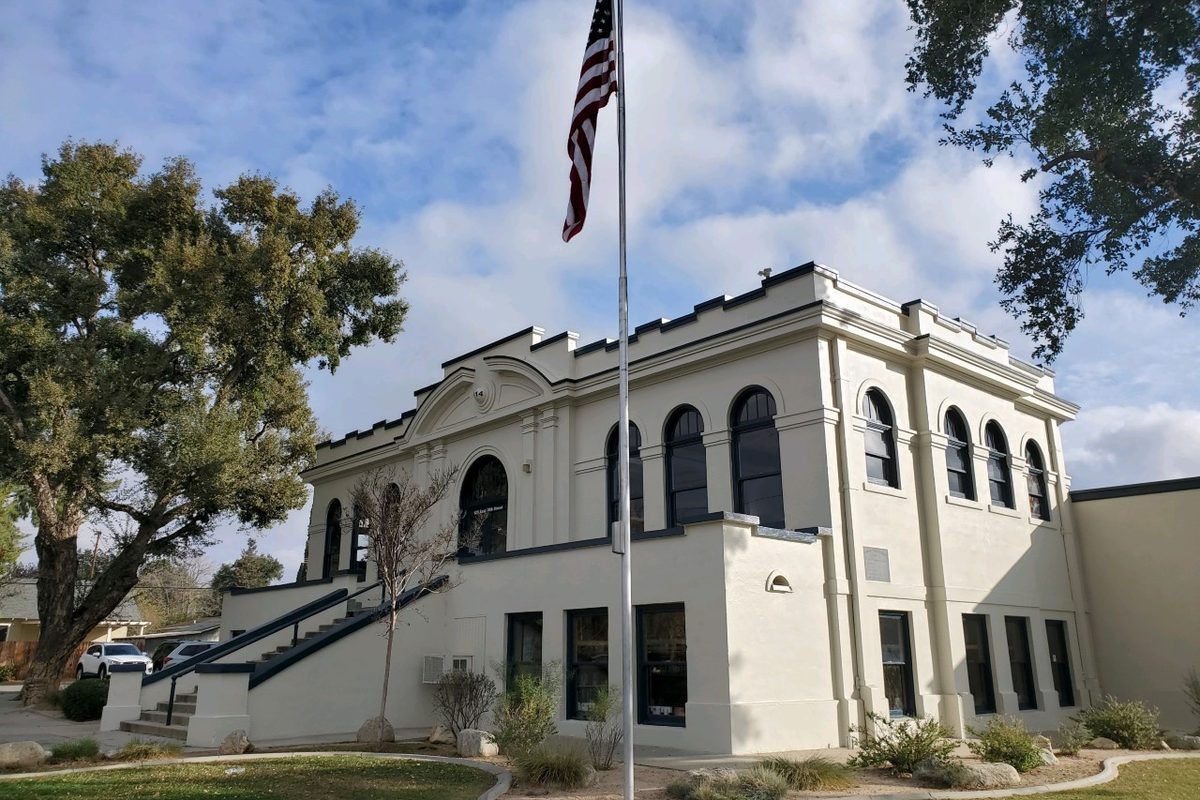 The white two-story Beaumont Library District building with tall arched windows and a flagpole flying the US flag