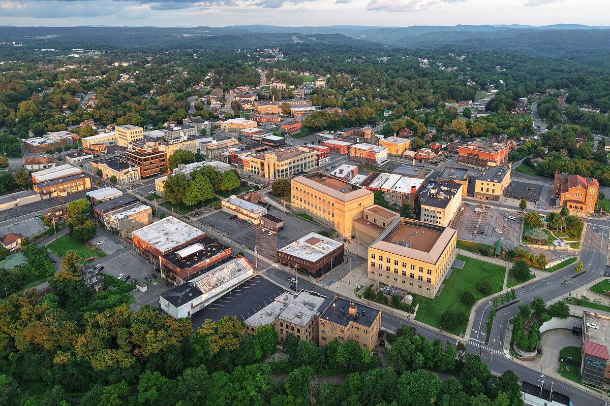 Aerial view of downtown Beckley at dusk, with brick and tan office blocks, parking lots and tree-covered hills stretching to the horizon