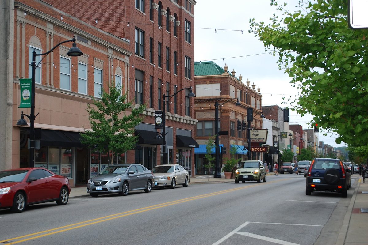 Main Street in Belleville, with red brick storefronts, black street lamps and green banners, cars parked along the curb and a Lincoln theater sign down the block