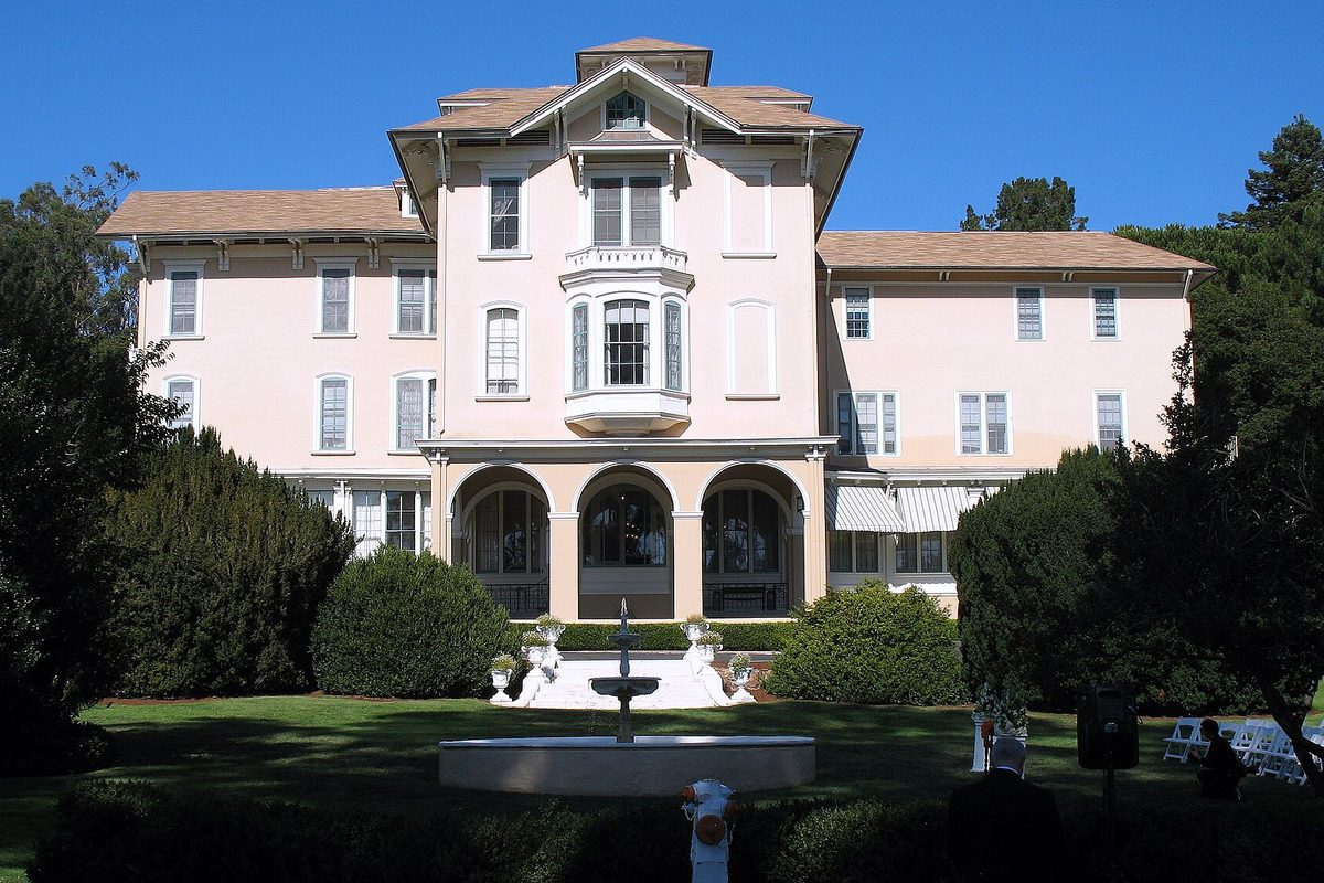 The pink Italianate William C. Ralston House in Belmont, three stories with arched ground-floor windows, a fountain and a green lawn in front, and dark trees on each side
