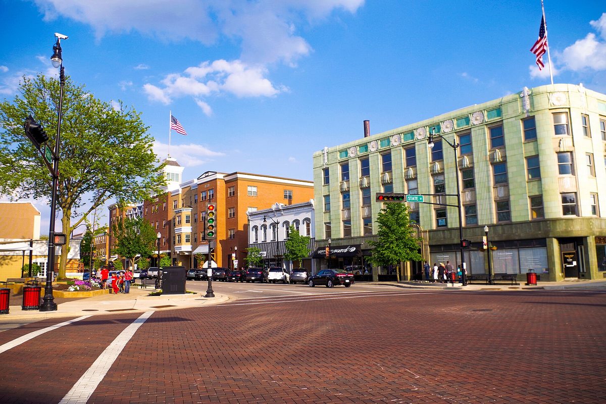 A brick-paved downtown Beloit intersection with a green-trimmed corner building, brick storefronts and an American flag