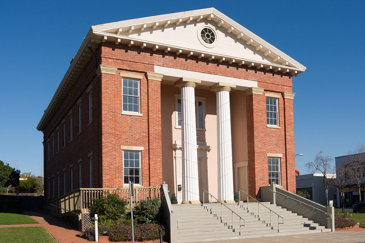 The red-brick Benicia Capitol building with two tall white columns, a triangular pediment and wide front steps under a blue sky