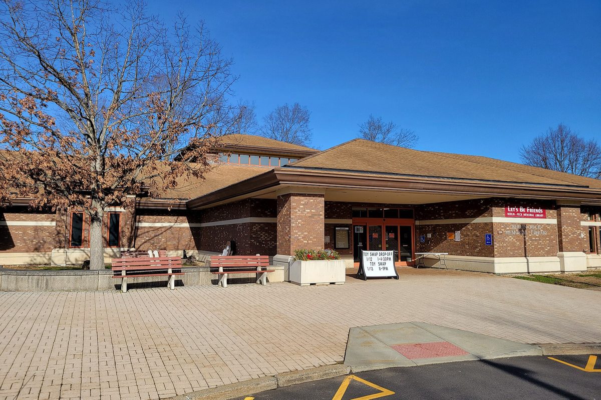 The Berlin-Peck Memorial Library, a low brick building with a wide brown roof, red benches and a planter out front, under a blue sky with bare trees