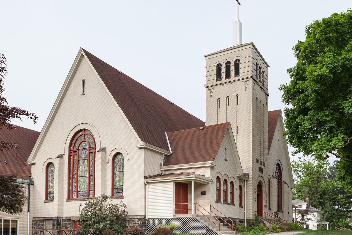Bethel Presbyterian Church in Bethel Park, a cream building with a brown roof, a tall square bell tower and arched stained-glass windows, framed by green trees