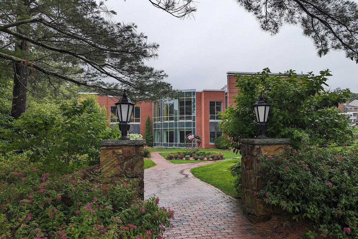 A brick path running between stone gateposts topped with black lanterns at Endicott College in Beverly, toward a brick and glass building