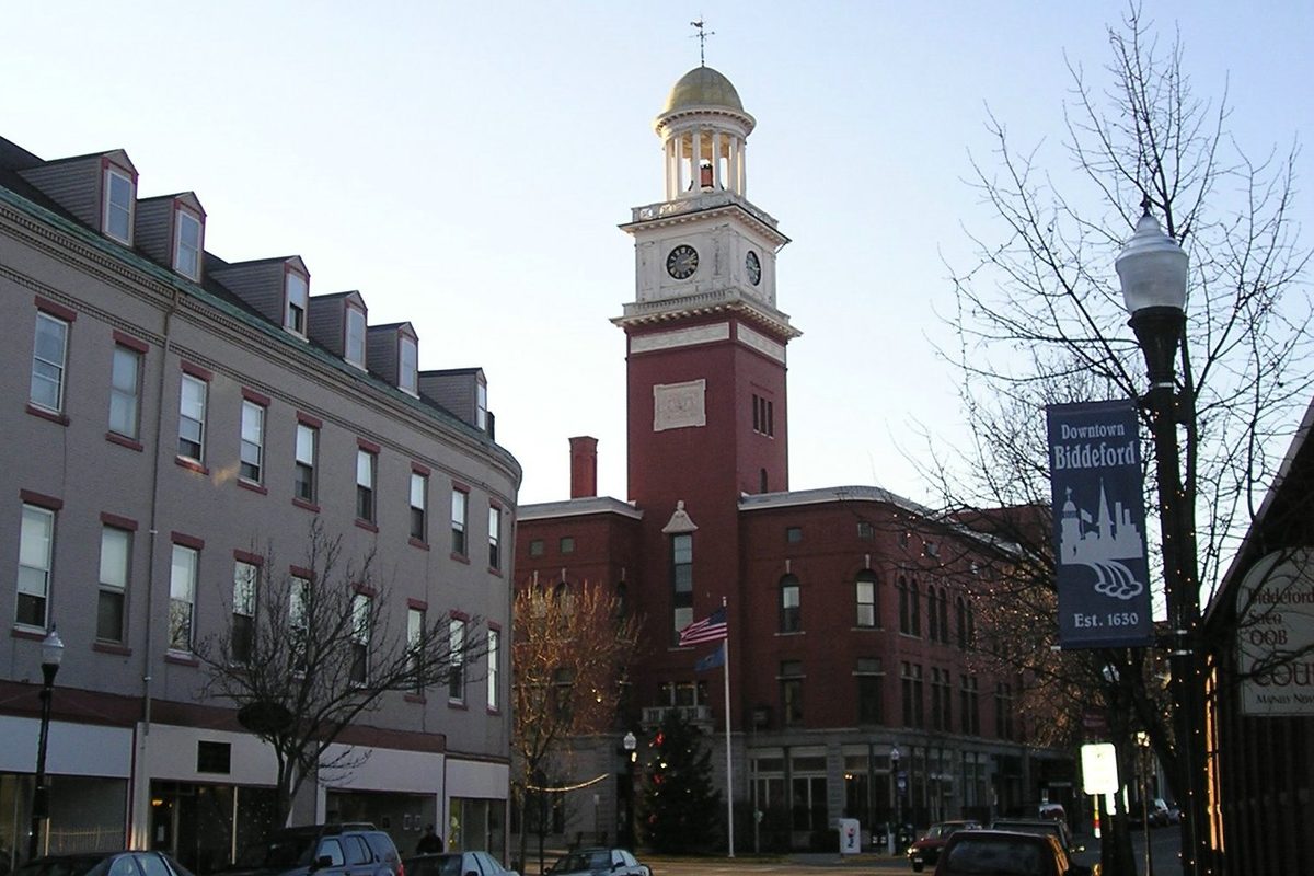 Biddeford City Hall, a red brick building with a white clock tower and gold dome, beside a Downtown Biddeford street banner