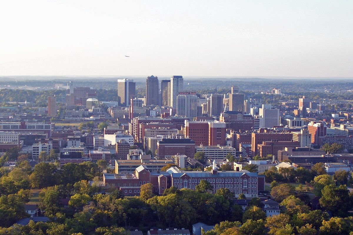 Downtown Birmingham's towers and brick buildings rising beyond a band of green trees, seen from high on Red Mountain