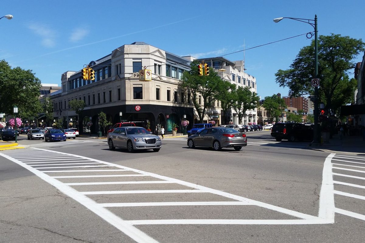 A cream-colored corner building with shops at a downtown Birmingham intersection, cars waiting at a white-striped crosswalk on a sunny day