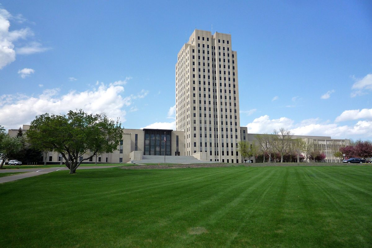 The pale stone tower of the North Dakota State Capitol in Bismarck behind a wide, freshly mowed green lawn under a blue sky