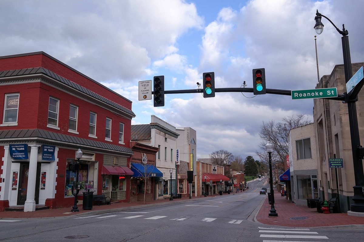 Red brick storefronts and a traffic signal at the Roanoke Street corner in downtown Blacksburg under a cloudy sky