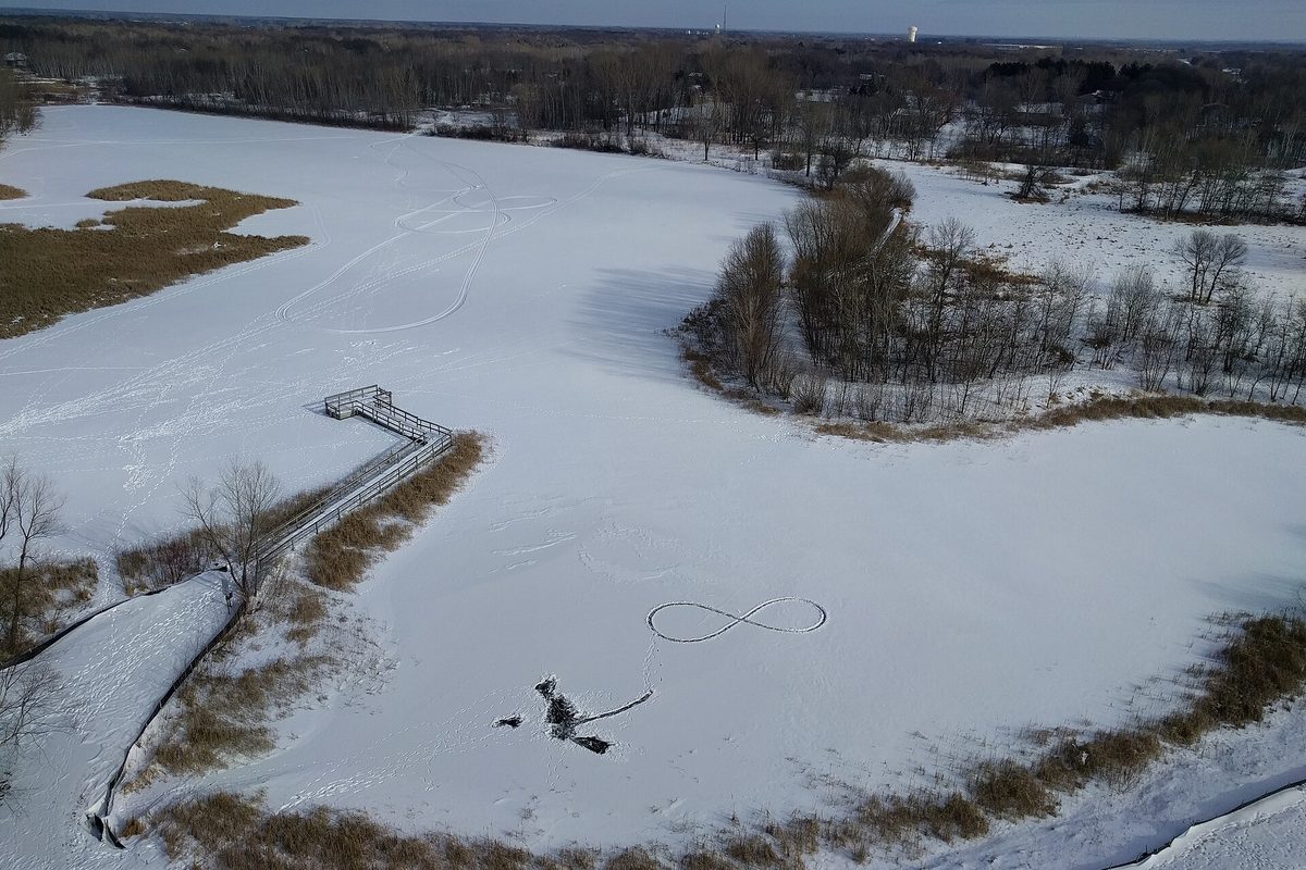 Aerial winter view of frozen, snow-covered Lochness Lake in Blaine, with a wooden boardwalk, cattails and tracks drawn in the snow