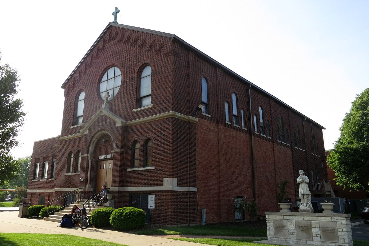 Saint Isidore Catholic Church in Bloomingdale, a tall red brick building with arched windows, a round window and a cross on the gable, with a white statue on a stone base out front