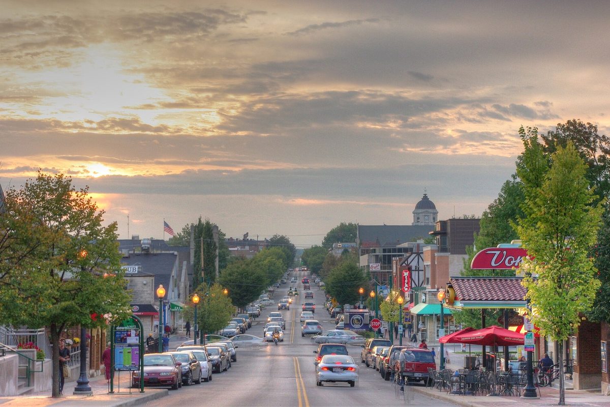 Kirkwood Avenue in Bloomington at sunset, with parked cars along both curbs, shop awnings and a domed tower at the far end of the street