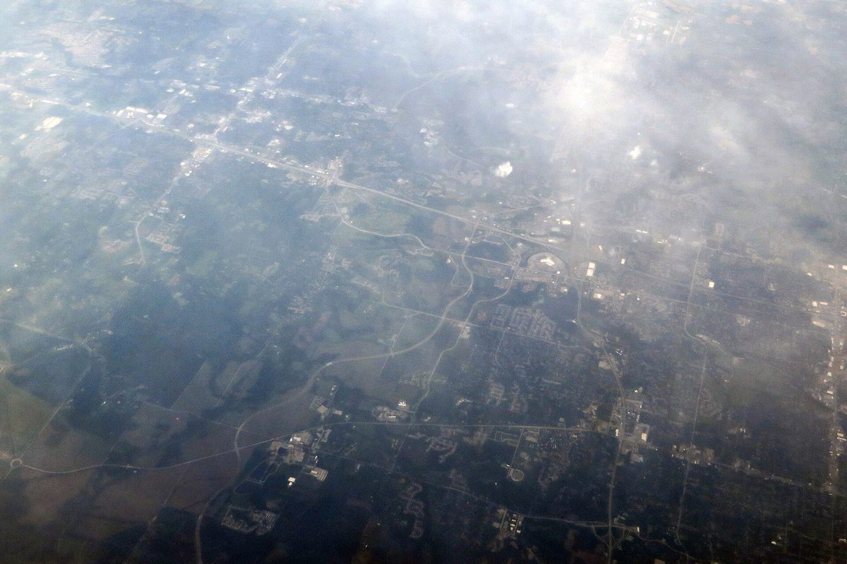 Aerial view of Blue Springs through haze, with roads, neighborhoods and green fields spread out below