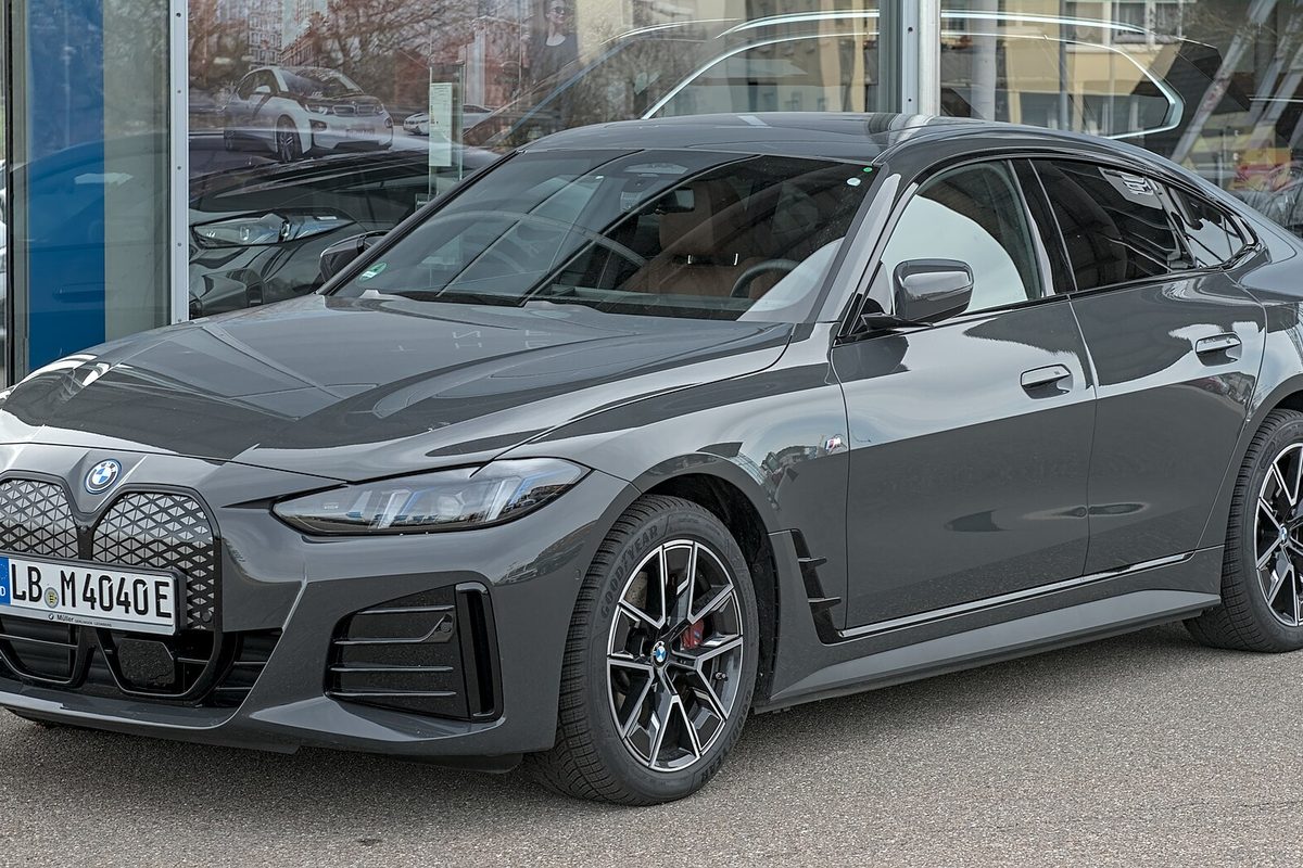 A dark gray BMW i4 Gran Coupe parked in front of a car showroom window, seen from the front left