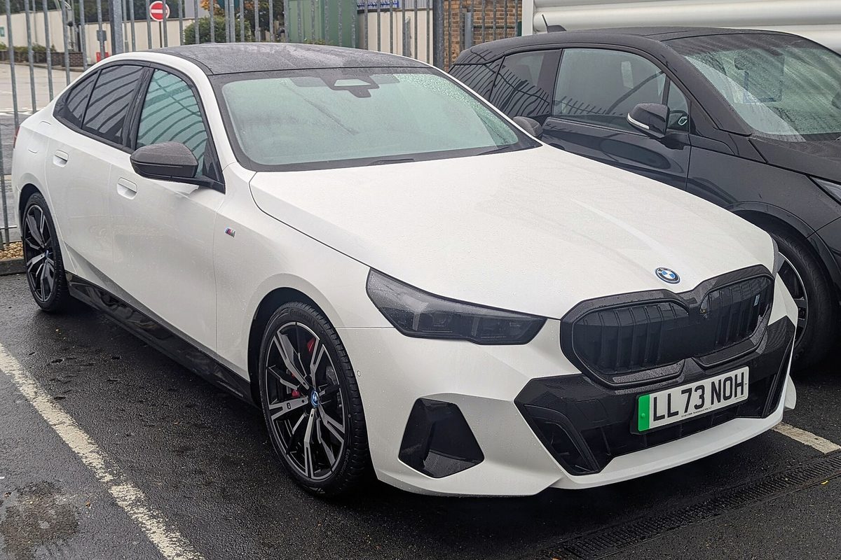 A white BMW i5 sedan with dark wheels and a black grille parked on wet pavement