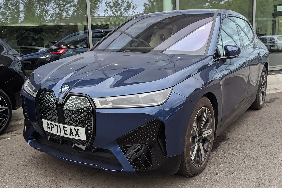 A dark blue BMW iX electric SUV with its large closed grille, parked outside a glass-fronted showroom