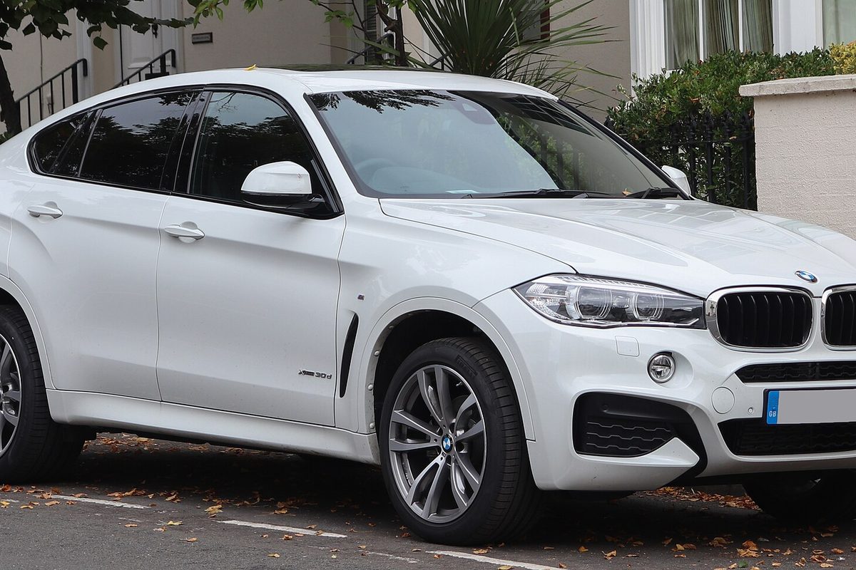 A white second-generation BMW X6 with M Sport bumpers, parked at a curb on a leafy street