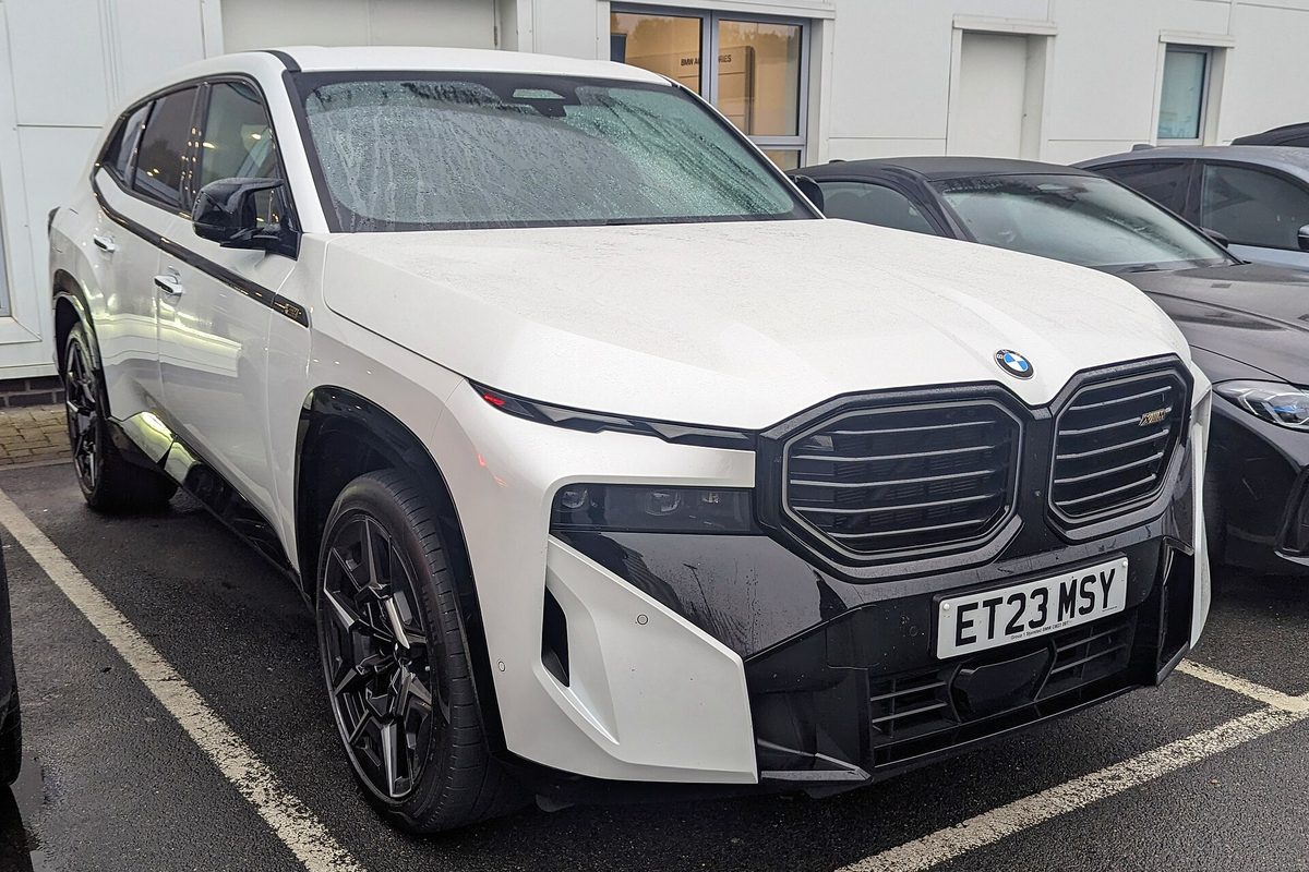 A white BMW XM SUV with a black two-part grille parked in a lot on a rainy day