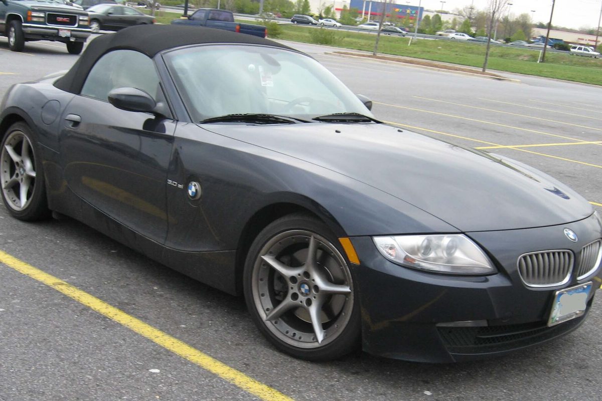 A dark gray BMW Z4 roadster with its black soft top up and five-spoke wheels, parked in a lot