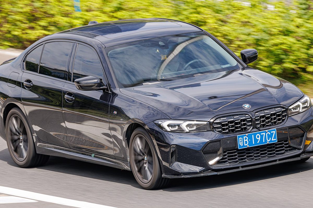 A dark blue long-wheelbase BMW 3 Series sedan of the G20 generation driving past a green hedge in China