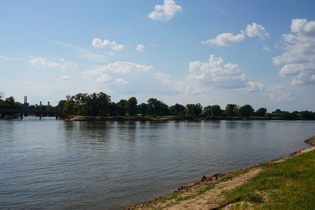 The wide Red River meeting Twelve Mile Bayou under a blue sky with white clouds, seen from a grassy bank in Bossier City