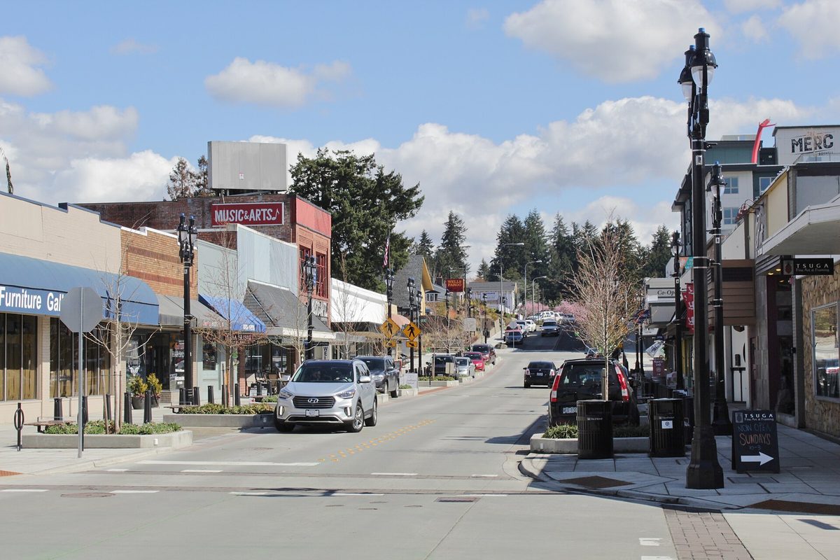 Main Street in downtown Bothell looking east, with low storefronts under awnings, black street lamps, parked cars and tall evergreens behind