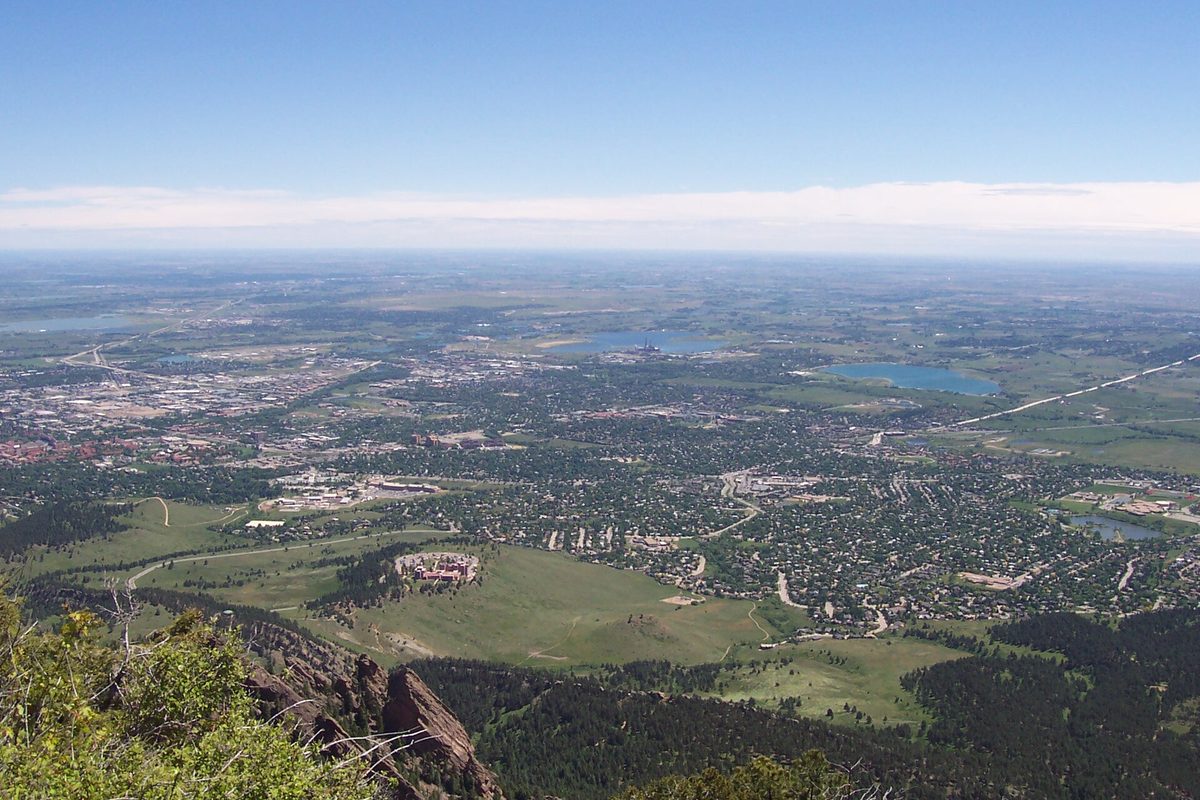Boulder seen from high on Bear Peak, the city spread across the plains below green foothills and red rock, with reservoirs in the distance