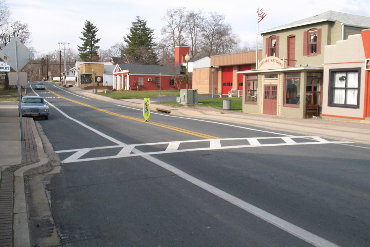 MD 564 at Chapel Avenue in old Bowie: a crosswalk, an old sedan at the curb, a small antiques shop and a red brick building with garage bays