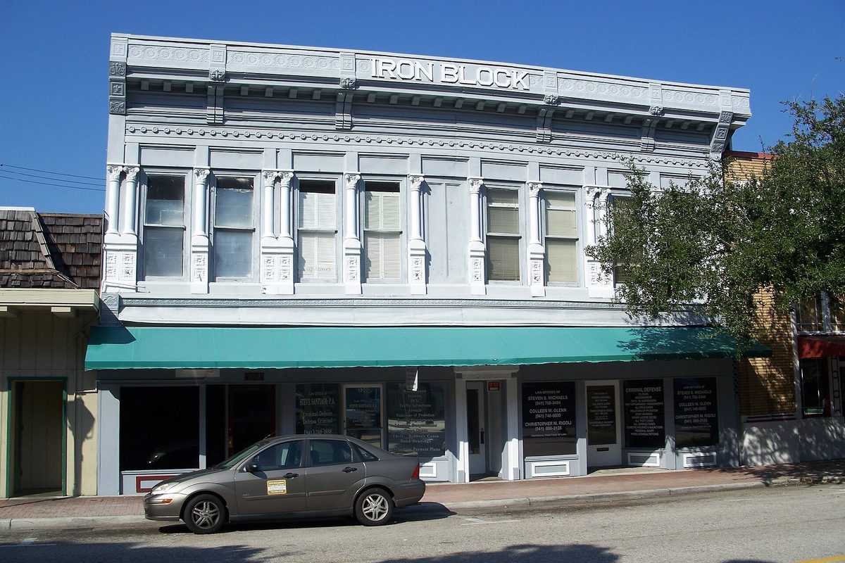 The two-story Iron Block Building in Bradenton, with ornate pale gray trim, a long green awning over the shopfronts and a small gray hatchback parked in front