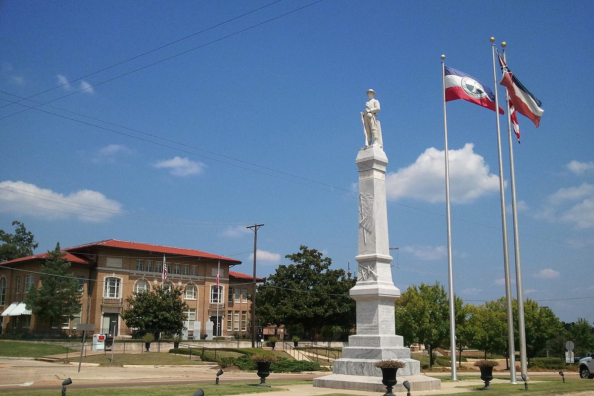 The Rankin County Confederate Monument with flags flying, the red-roofed historic courthouse behind it in Brandon