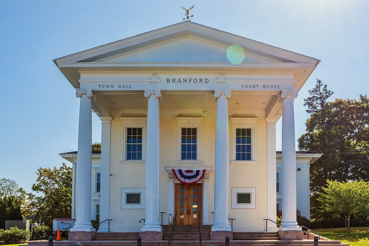 Branford's white Town Hall and Court House with tall columns and red, white and blue bunting over the front door, under a clear sky