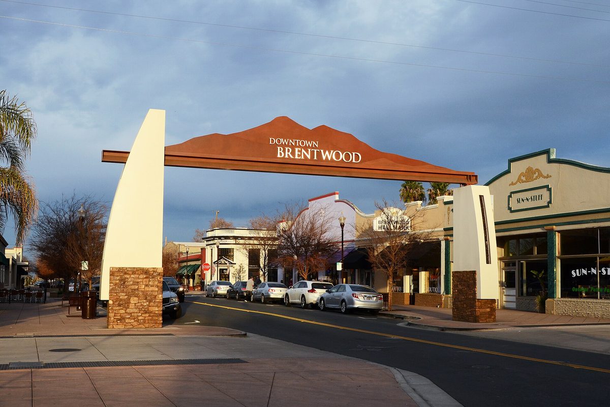The Downtown Brentwood arch over the street, with cars parked along the curb and shopfronts behind it under a cloudy evening sky
