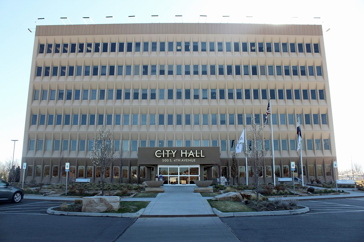 The six-story Brighton City Hall at 500 South 4th Avenue, with a rock-lined landscaped walkway and flags on poles out front