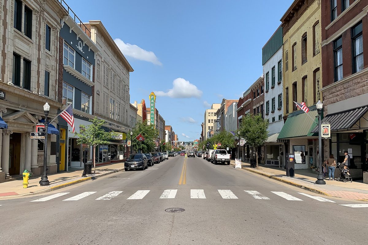 State Street in downtown Bristol, with brick storefronts, American flags, a painted crosswalk and a tall vertical theater sign under a blue sky