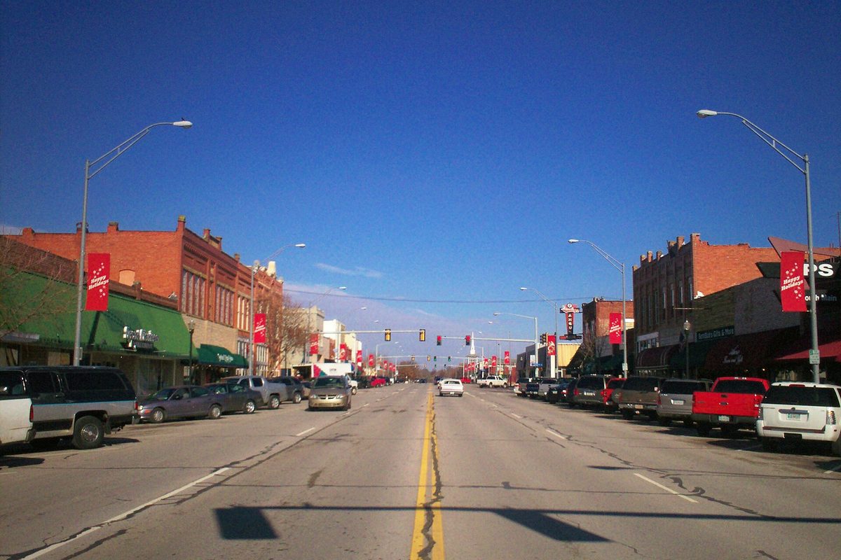 Looking north up Main Street in downtown Broken Arrow, with brick storefronts, red banners on the light poles and pickups parked along both curbs