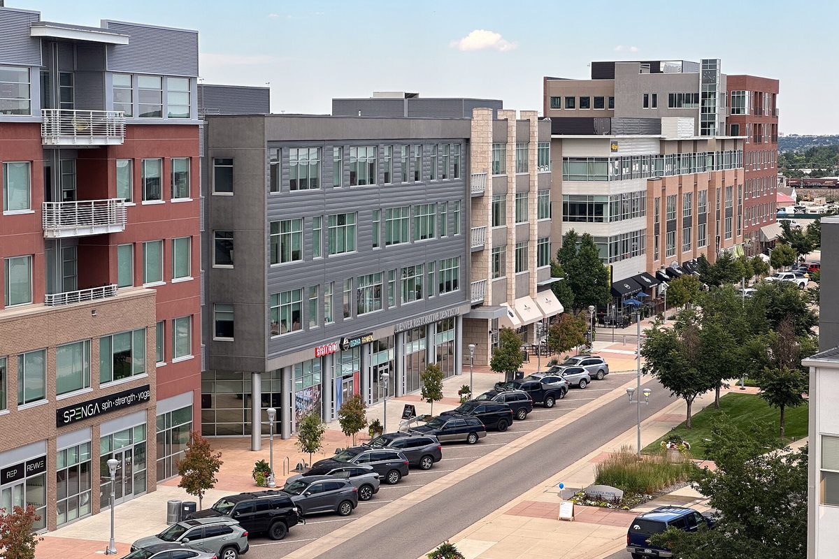 Four- and five-story brick and gray mixed-use buildings along a street at Arista Place in Broomfield, with cars parked along the curb