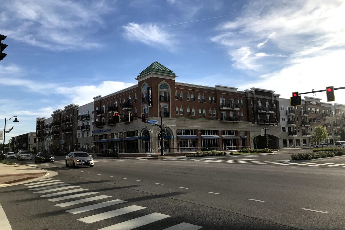 The Arbuckle in Brownsburg, a four-story brick building with a green-roofed corner tower, seen across a crosswalk under a blue sky