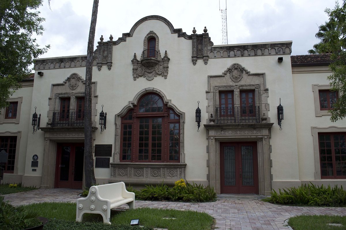 The ornate white former Southern Pacific depot in Brownsville, now the Brownsville Historical Museum, with carved stone trim, red wooden doors, small iron balconies and a white bench on the front walk