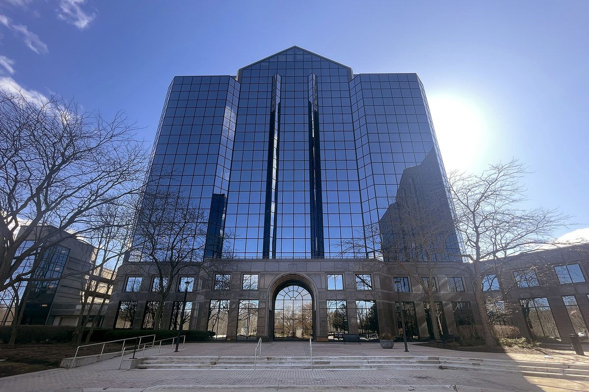 A tall mirrored-glass office tower with an arched stone entrance and bare trees, the sun low in a blue sky, at the former Zenith Data Systems headquarters