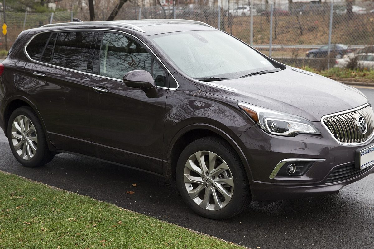 A dark brown 2016 Buick Envision compact SUV with chrome grille parked at a curb beside a strip of grass