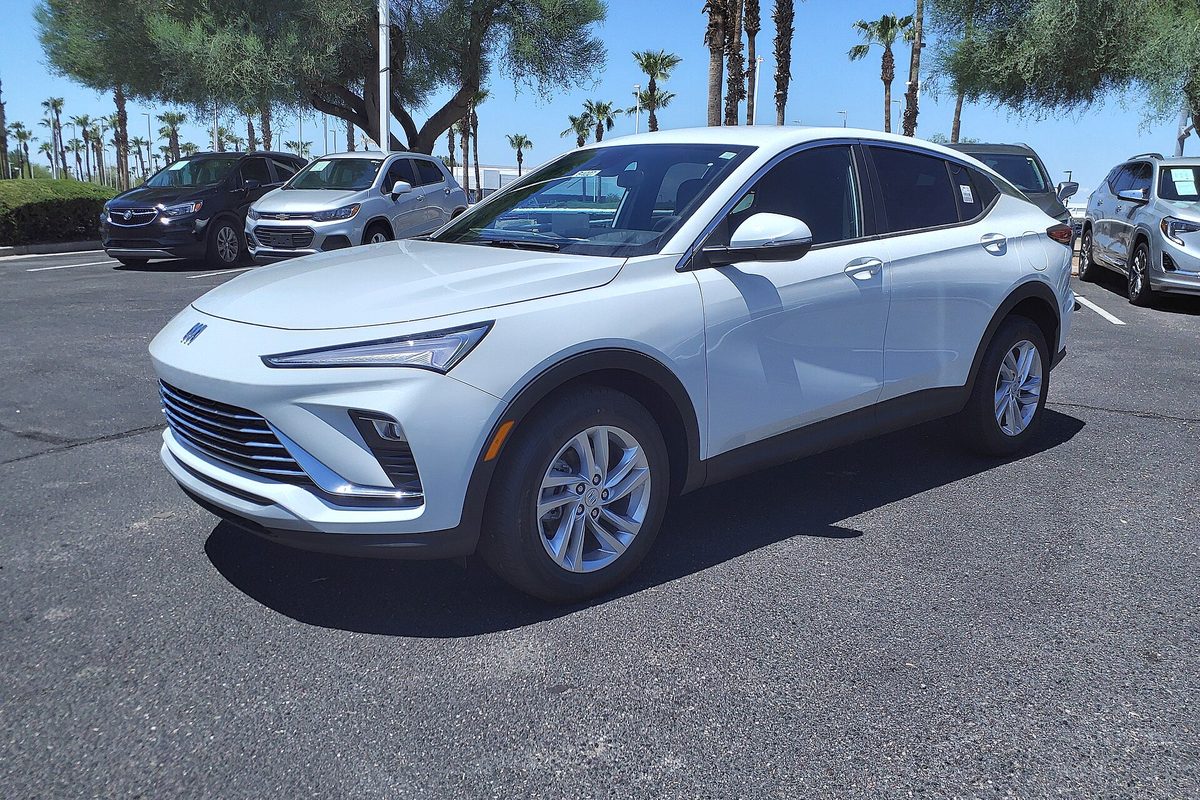 A white 2024 Buick Envista crossover with a sloping roofline parked on a dealer lot under palm trees