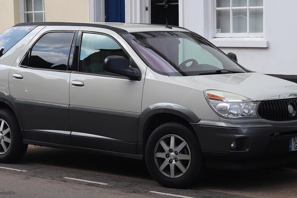 A 2004 Buick Rendezvous crossover in silver with dark gray lower panels, parked at a curb in front of a white house