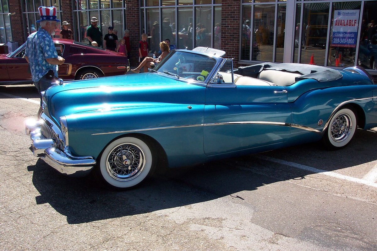 A turquoise 1953 Buick Skylark convertible with whitewall tires and wire wheels at an outdoor car show