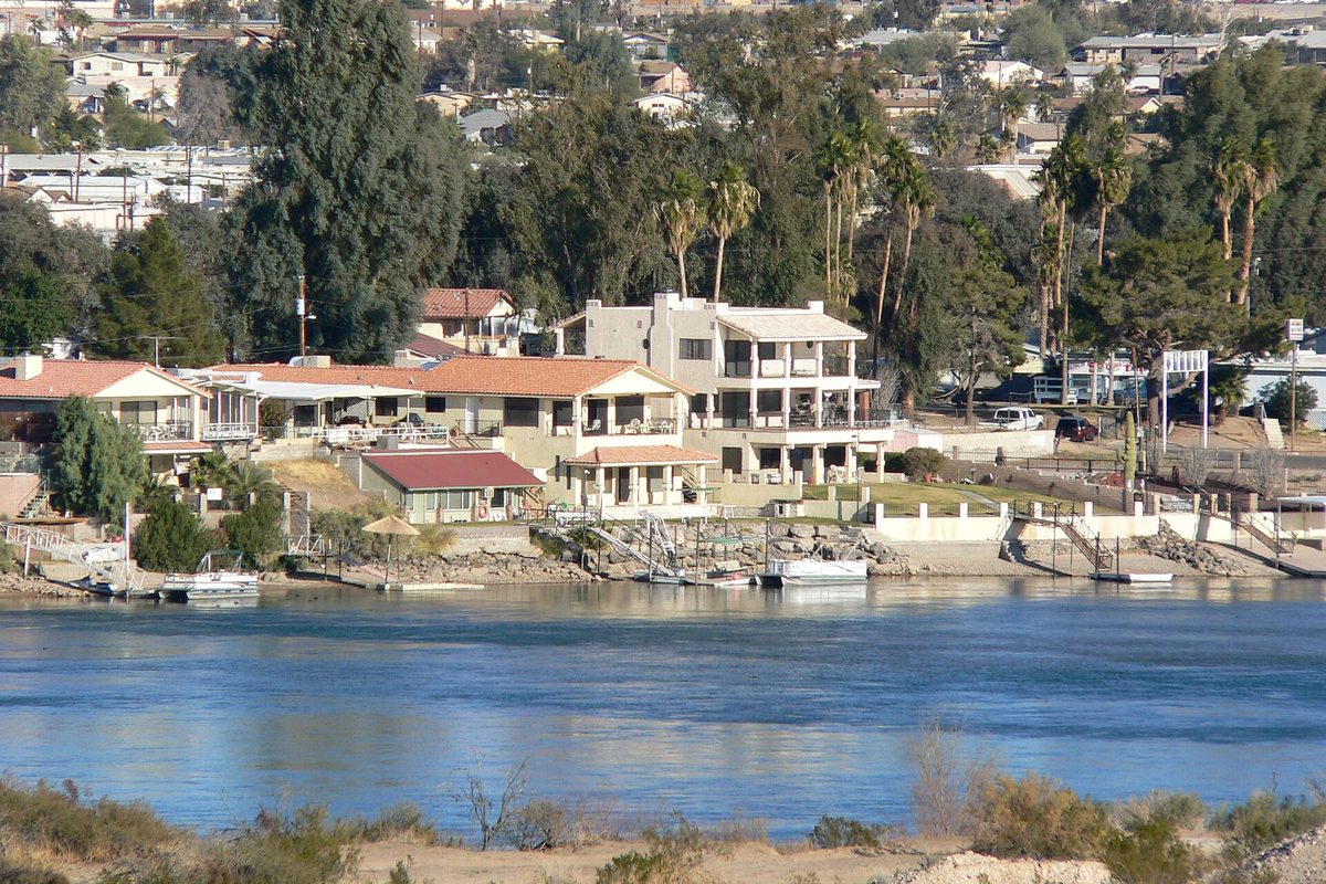 Tile-roofed homes and palm trees on the Colorado River shore in Bullhead City, seen across the water from the Nevada side