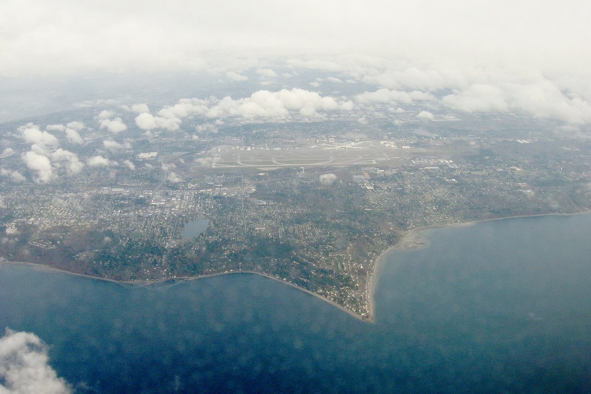 Aerial view through clouds of Three Tree Point jutting into Puget Sound, the Burien shoreline around it and the runways of Seattle-Tacoma International Airport behind