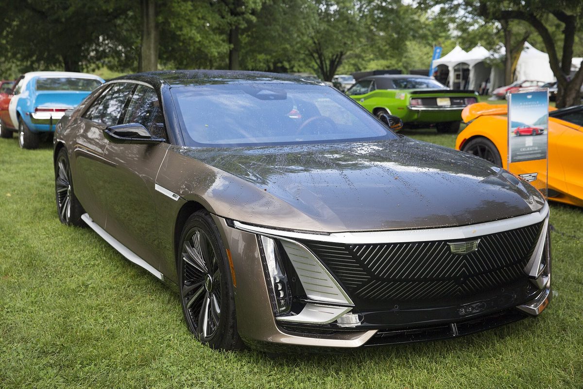A bronze Cadillac Celestiq with a black roof, black mesh grille and thin vertical headlights, parked on grass at an outdoor car show