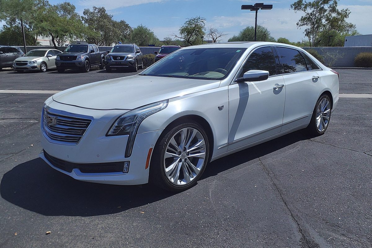 A pearl white Cadillac CT6 sedan, front three-quarter view, parked in a sunny lot with pickups behind it