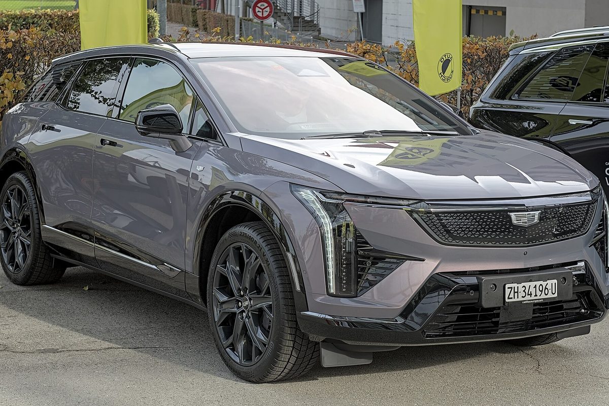 A dark gray Cadillac Optiq electric crossover with black wheels, front three-quarter view, at an outdoor car show
